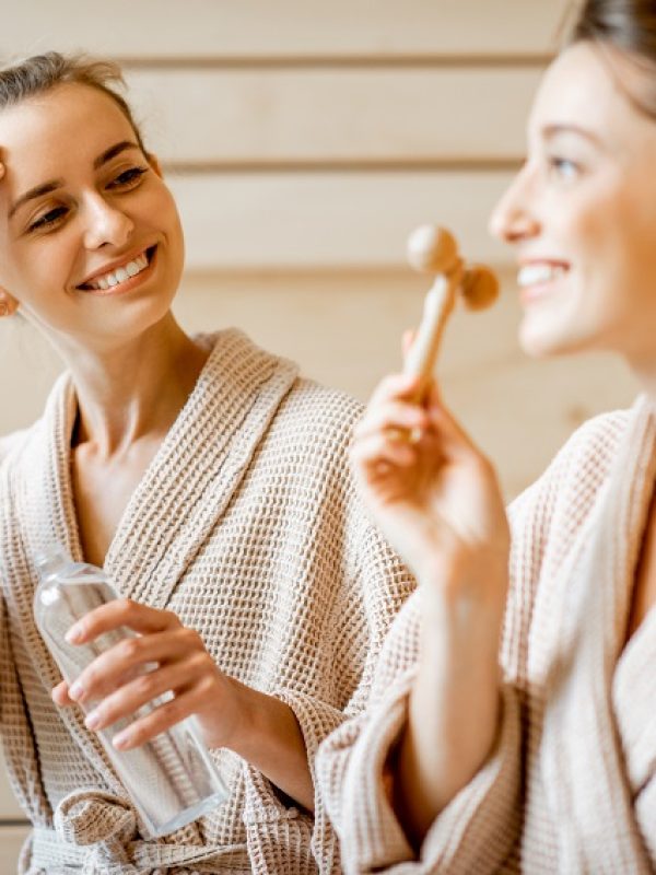 Young women taking care of their skin, making facial massage in the SPA, sitting together in bathrobes